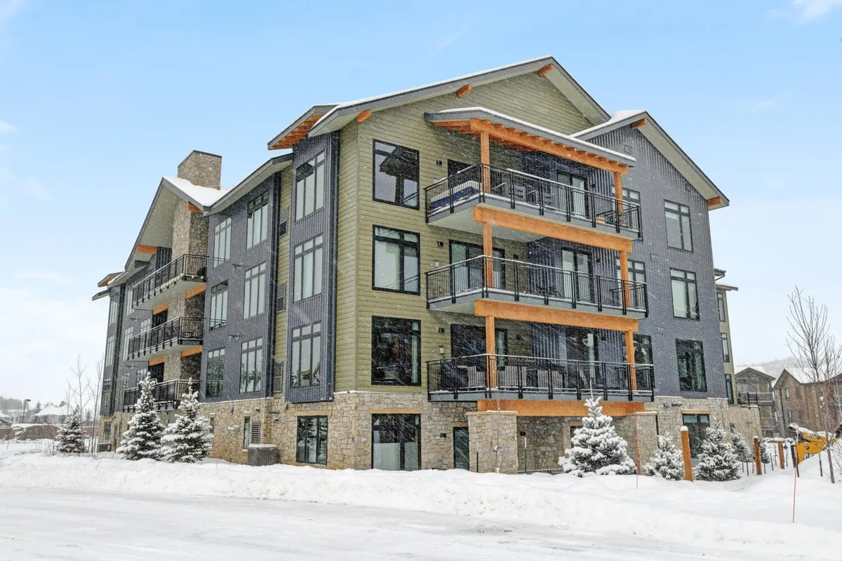 A contemporary exterior of the condo complex, with modern architecture, large windows, balconies, and a snow-covered landscape. The building exudes a welcoming ambiance, hinting at a range of recreational opportunities nearby.