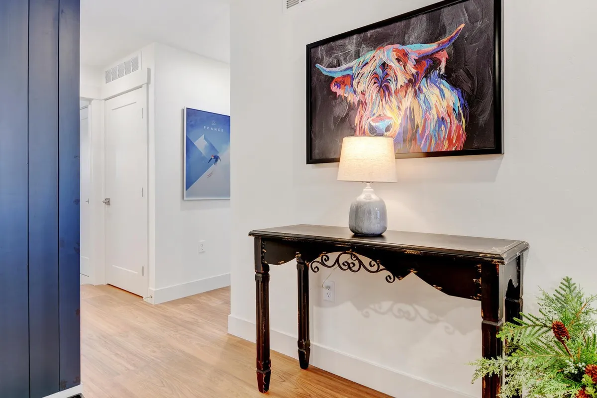 This shot features a console table adorned with a colorful cow artwork and a table lamp, creating a warm, inviting ambiance that hints at shared moments and lively conversations within the home.