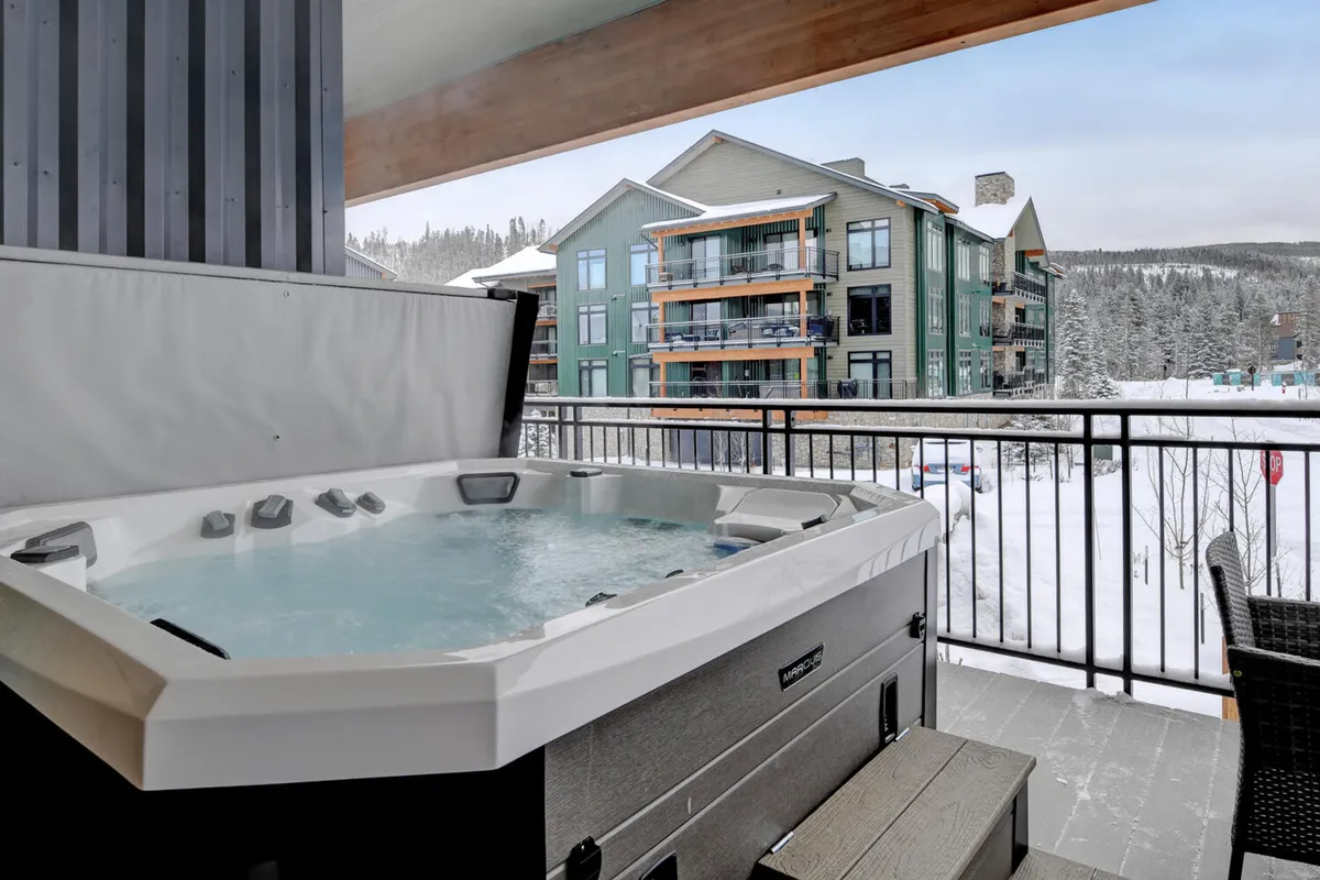 A scenic balcony hot tub set against a snowy mountain landscape, with a sturdy railing framing the view. The inviting hot tub is perfect for relaxing after a day of family recreation or local adventure.