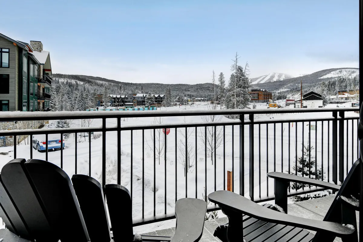 A cozy balcony scene featuring Adirondack chairs facing a snowy landscape and majestic mountain backdrop. The balcony railing frames the picturesque view, suggesting a space perfect for unwinding and appreciating the natural beauty firsthand, whether enjoying a morning coffee or an evening drink.