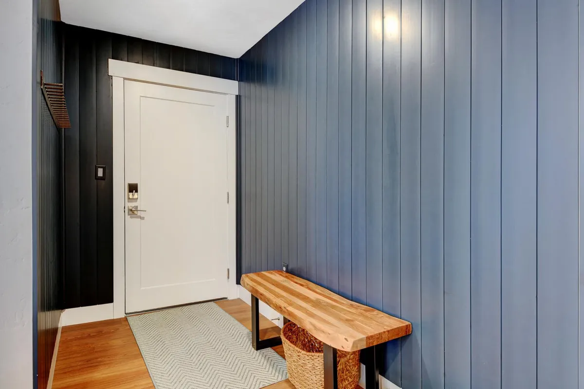 This image captures the entryway of the property, featuring a wooden bench, blue vertical paneling, and a white door. The entryway feels cozy and inviting, setting the tone for welcoming friends and family as they arrive for group get-togethers.