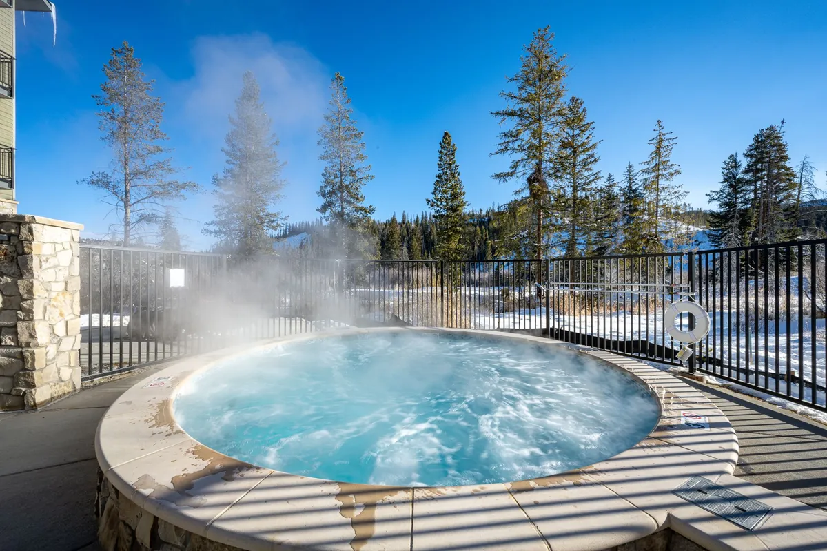 An exterior shot of a hot tub nestled among trees with a panoramic mountain view in the background, emphasizing connection to nature and outdoor leisure space.