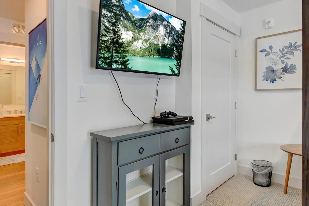 A cozy living area with a television displaying a mountain landscape, a contemporary gray console table, and decorative wall art. The scene is perfect for relaxing together after a day of exploring, echoing the section’s mention of movie nights, gaming sessions, and group entertainment.